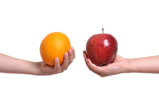 A pair of hands, one holding an apple, and another holding an orange.